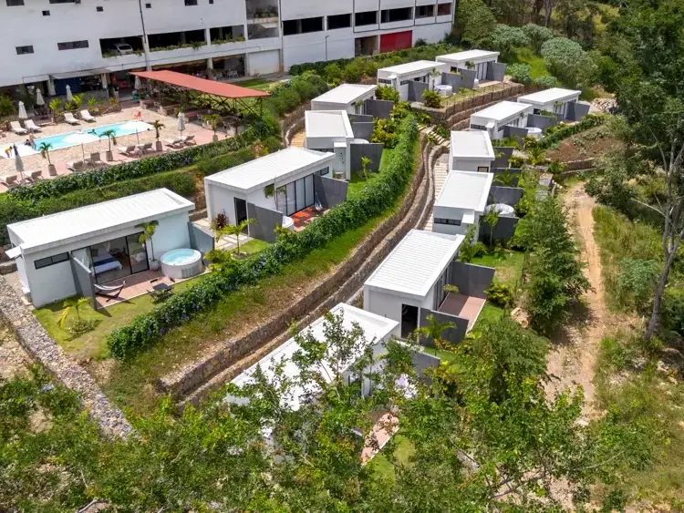 Vista de dron de las unidades blancas del glamping entre jardines y caminos