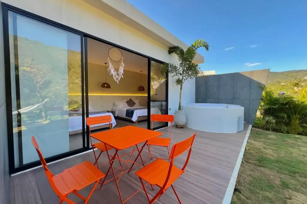 Jacuzzi blanco, mesa con sillas naranjas y ventanal abierto en la terraza de la unidad familiar del glamping
