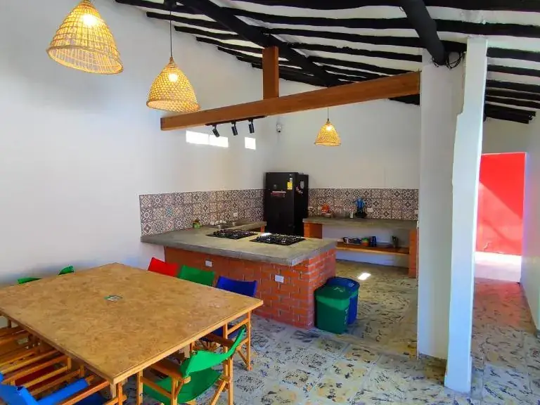 Cocina compartida de Origen con mesa larga de madera, sillas de colores y lámparas de mimbre
