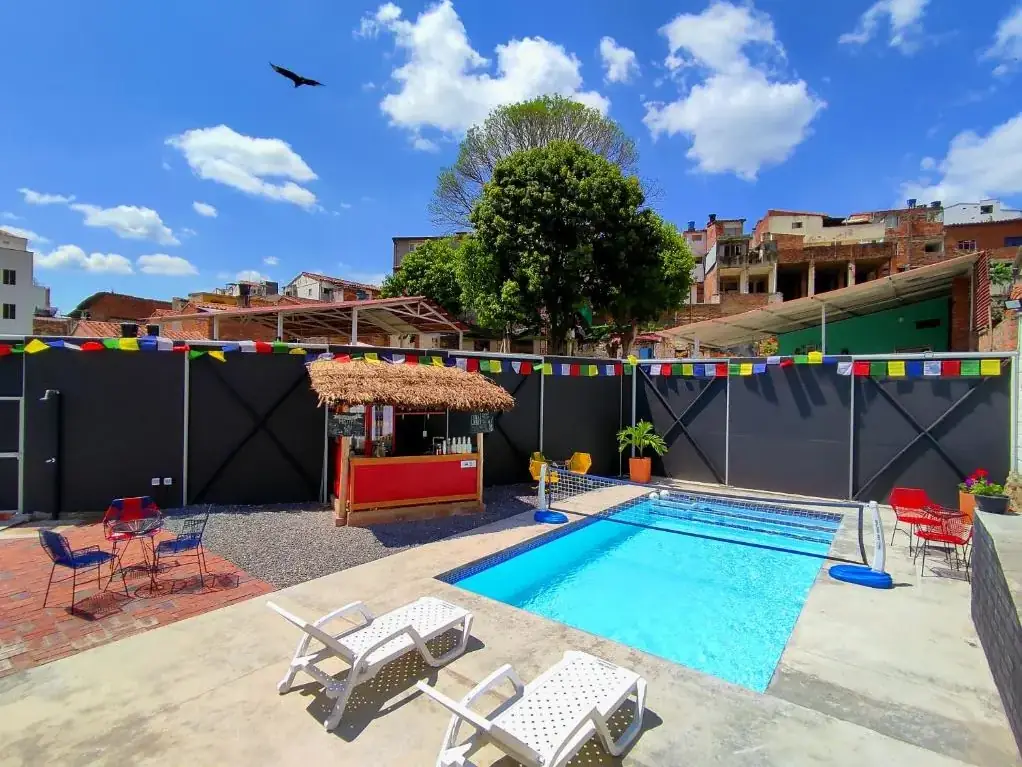 Piscina rectangular de Origen de día, con el bar y las mesas rojas al fondo