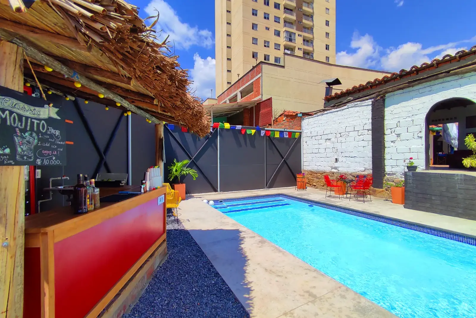 Piscina de Origen junto al bar de madera roja y techo de palma, con edificios de San Gil detrás
