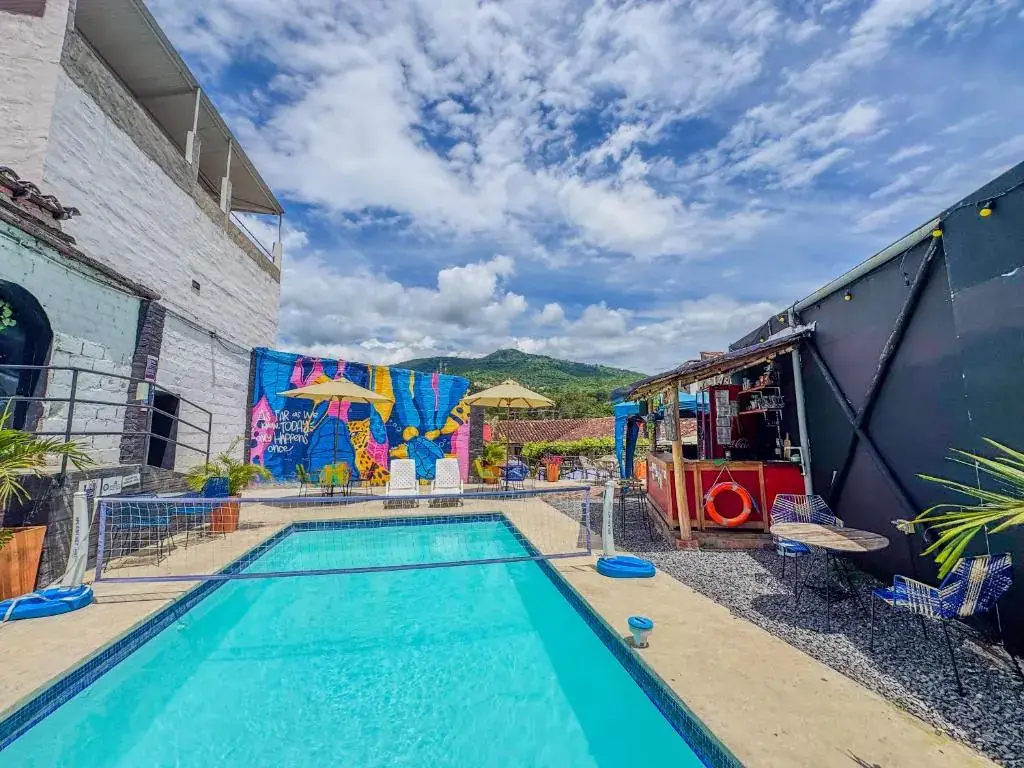 Piscina de Origen con un mural de colores al fondo y el bar a un lado, bajo el cielo azul