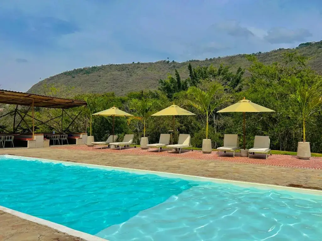 Piscina de Del Río con tumbonas y sombrillas amarillas, palmas y una montaña verde detrás