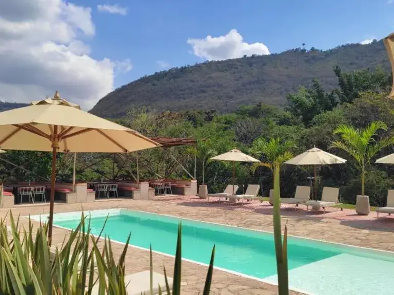 La piscina de Del Río de día, entre palmas, con la ladera verde detrás