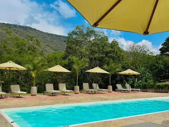 Tumbonas grises y sombrillas amarillas junto a la piscina de Del Río, con la montaña verde enfrente