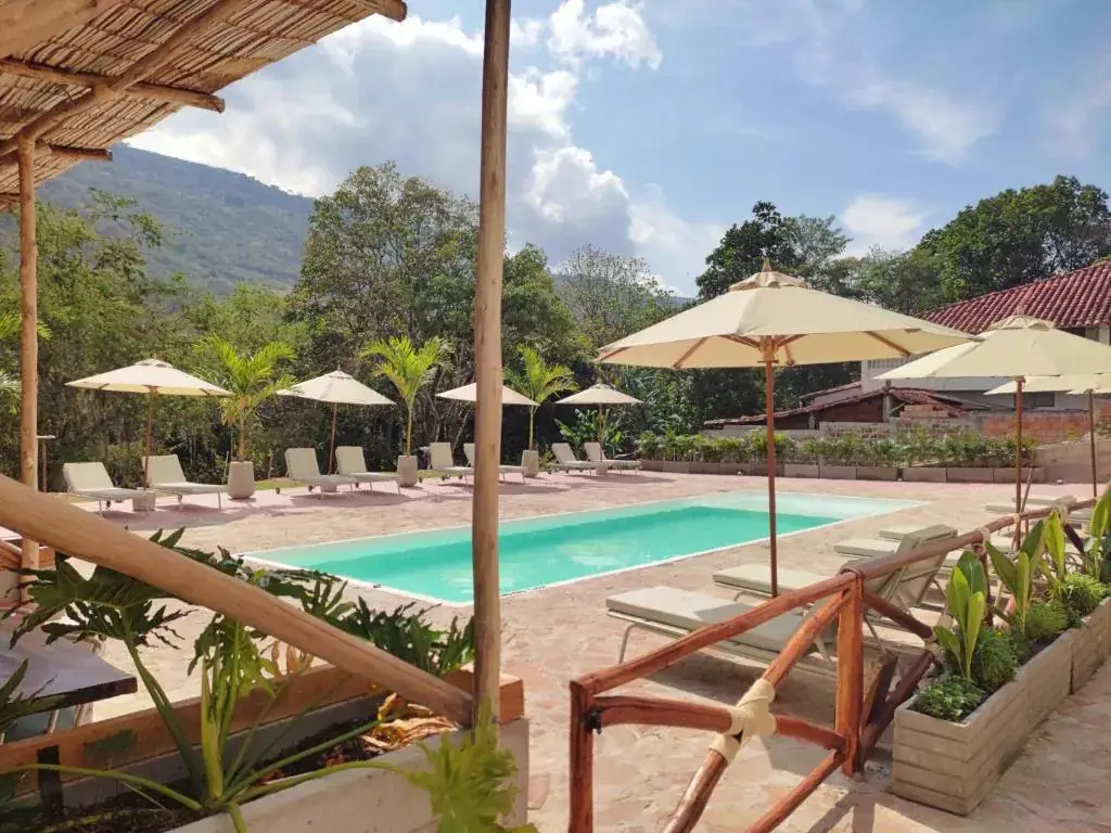 Parasoles blancos y tumbonas junto a la piscina, con barandas de madera y la montaña al fondo